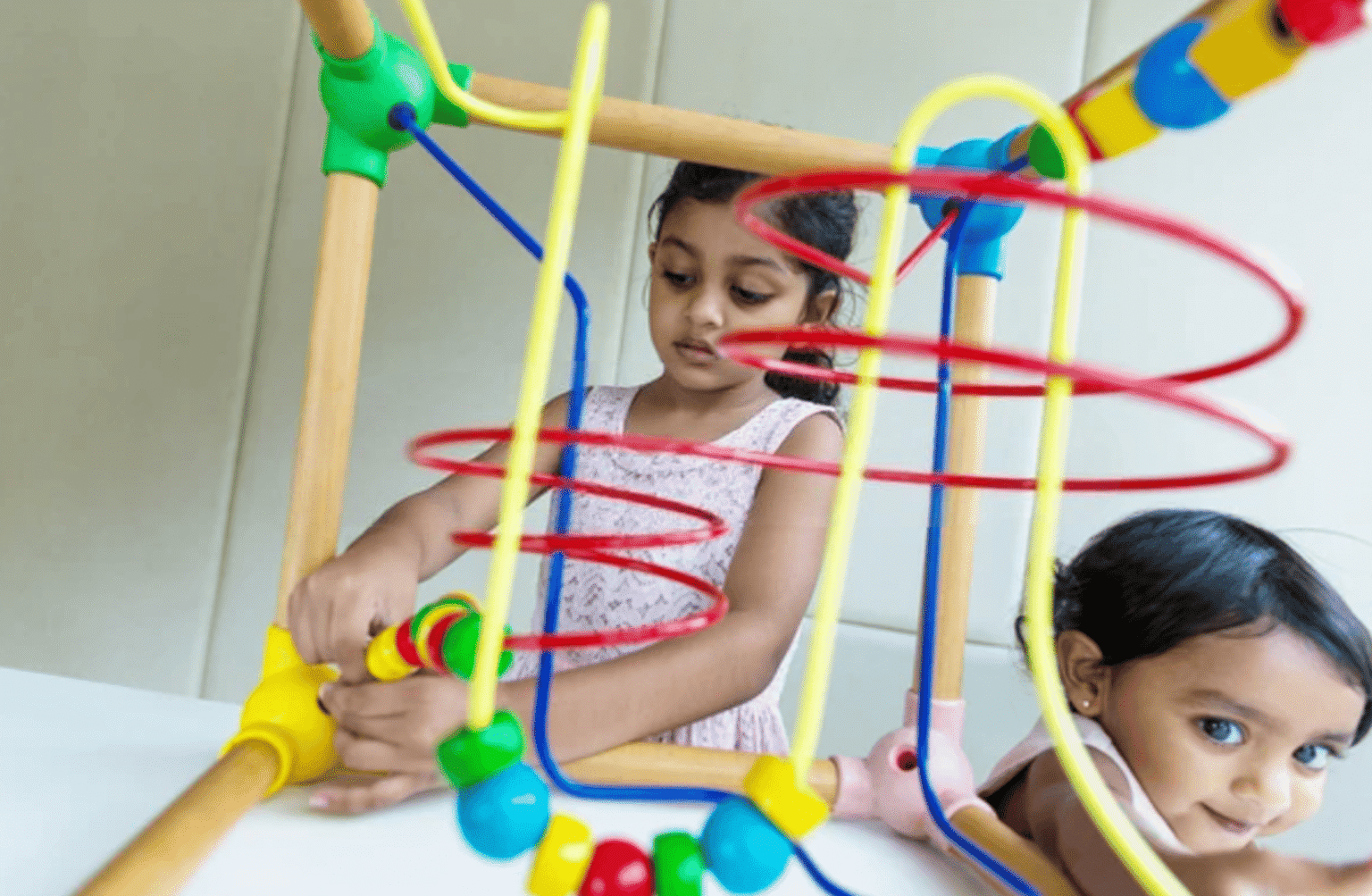 Young child in a green polo shirt playing on a colorful outdoor plastic climbing structure at a preschool.